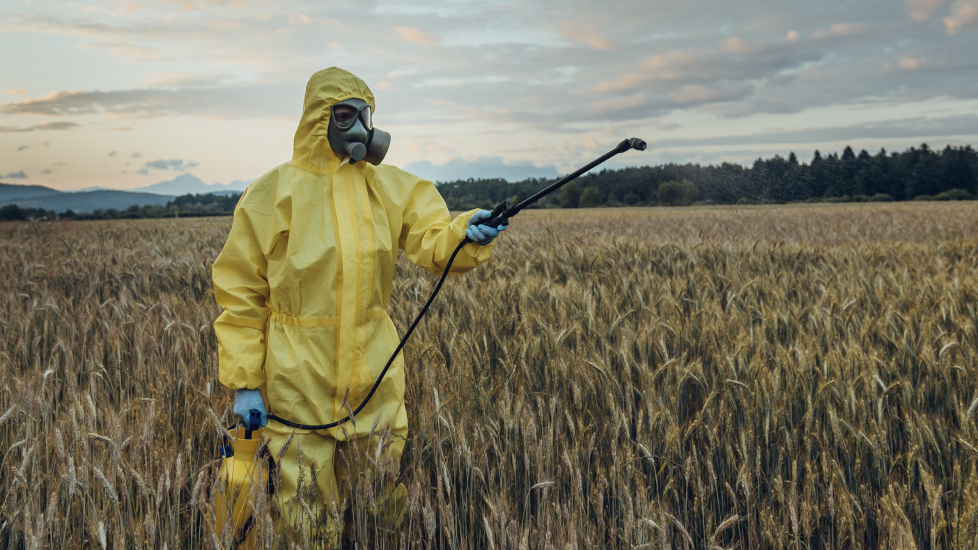 Person in suit spraying chemicals over crop fields